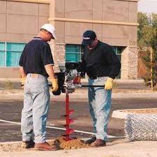 Two workers using a Ground Hog C-17-5 Two-Man Earth Drill on a street.