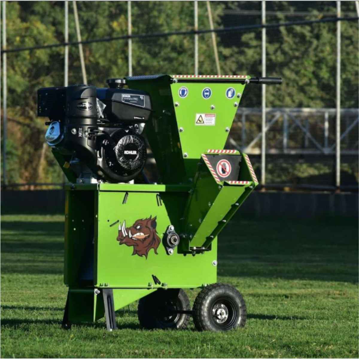 a green woodchipper on a sunny day on a grassy field with trees in the background