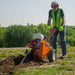 Man operating a brave 18 in. trencher in a field with greenery in the background