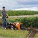 Man operating a brave 5 inch bed edger in a field with corn in the background