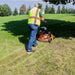 Person using a brave power rake dethatcher on a grassy field on a sunny day.
