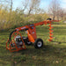 Orange Brave Towable Auger on grass with trees in the background