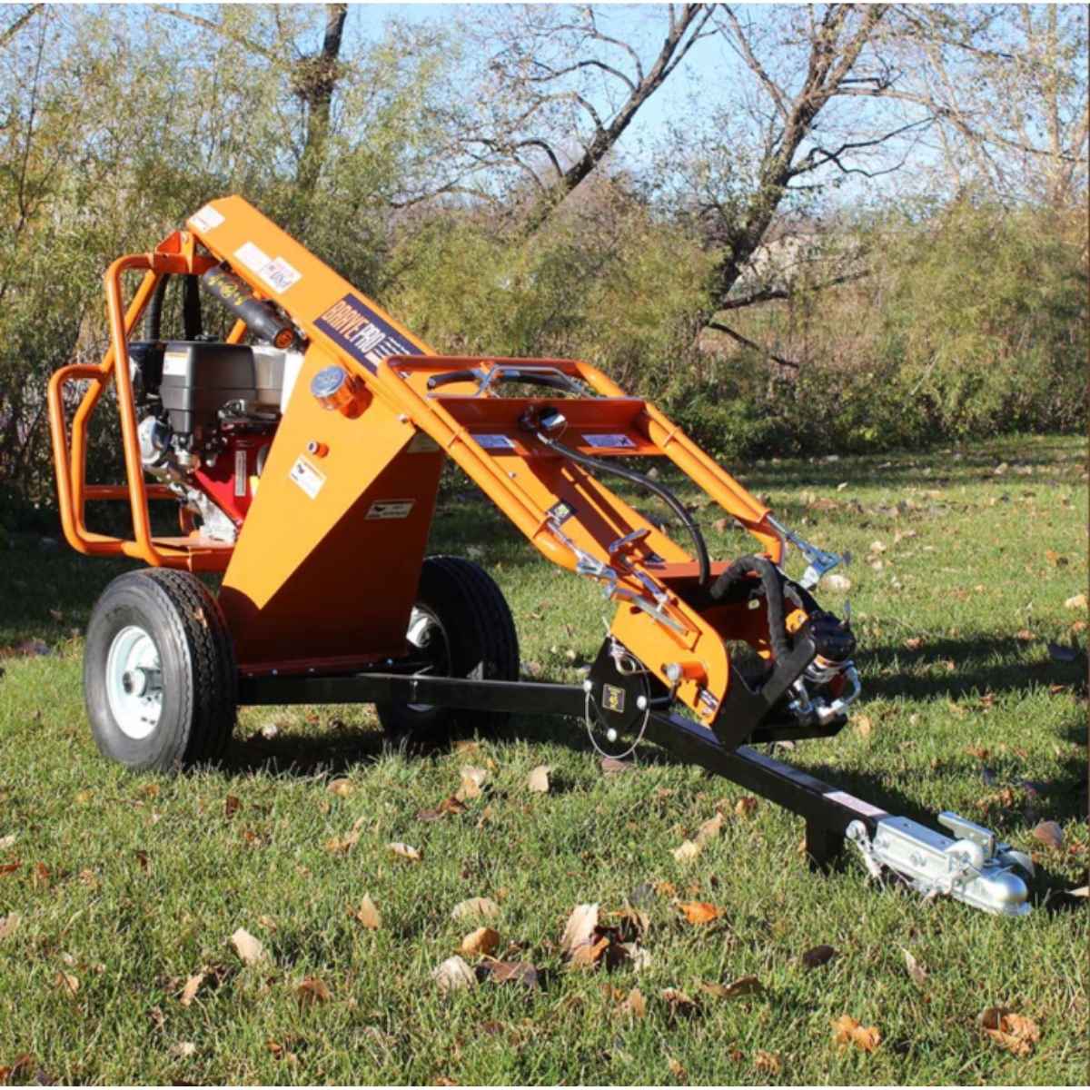 Orange Brave Towable Auger on a grassy area with trees in the background