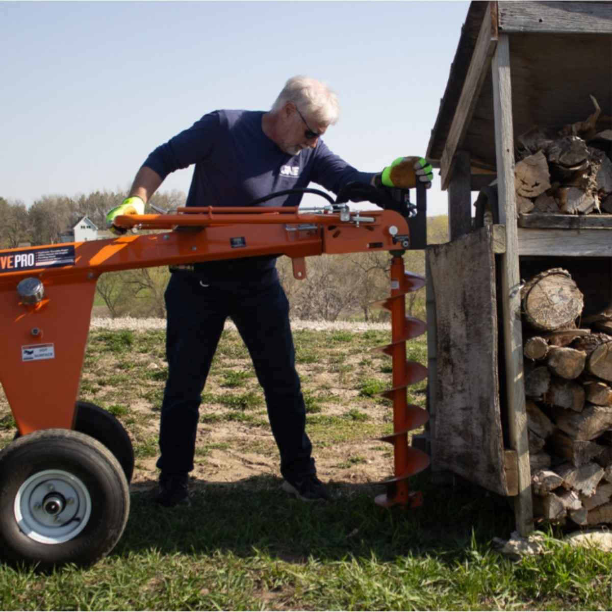 Man operating a Brave hydraulic Towable Auger in an outdoor setting with stacked logs nearby.