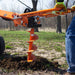 Person using an orange brave pro hydraulic auger to make a hole in the ground outdoors.