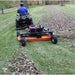 Person riding an ATV with a brave pro tow behind finish cut 60 inch mower attached to cut a grassy lawn covered in leaves