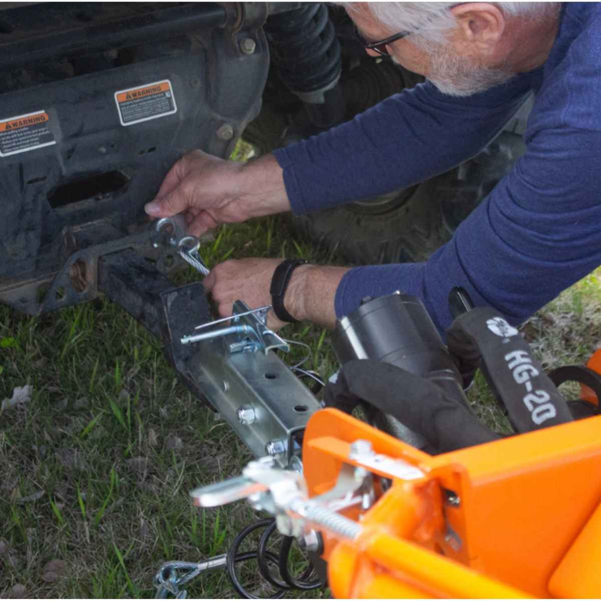 Person attaching a Brave hydraulic Auger tow bar to a vehicle on grass