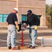 Two workers using a Ground Hog C-17-5 Two-Man Earth Drill on a street.