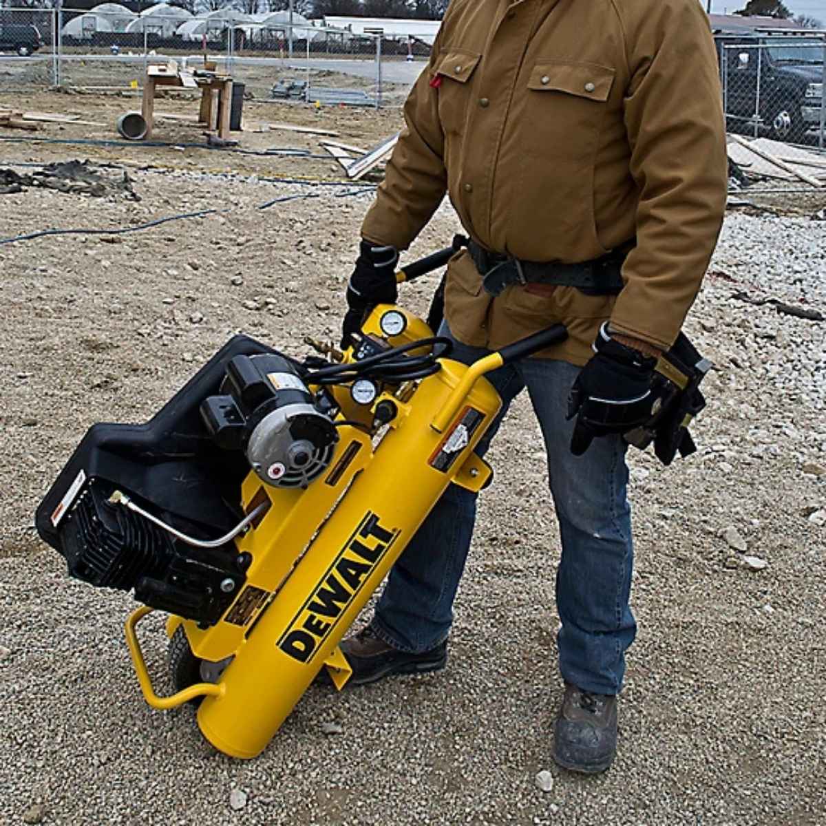 Person holding a yellow Dewalt 8 gal 5.7cfm wheelbarrow air compressor on a construction site
