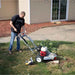Person using a dosko mini 6hp stump grinder on a grassy area outside a house.