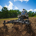Person operating an ATV with a GreyWolf till n Claw chisel plow & Cultivator attached in a field with trees and blue sky in the background