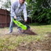 person operating a green georipper trencher in a grassy yard with a wooden fence in the background in the daytime.