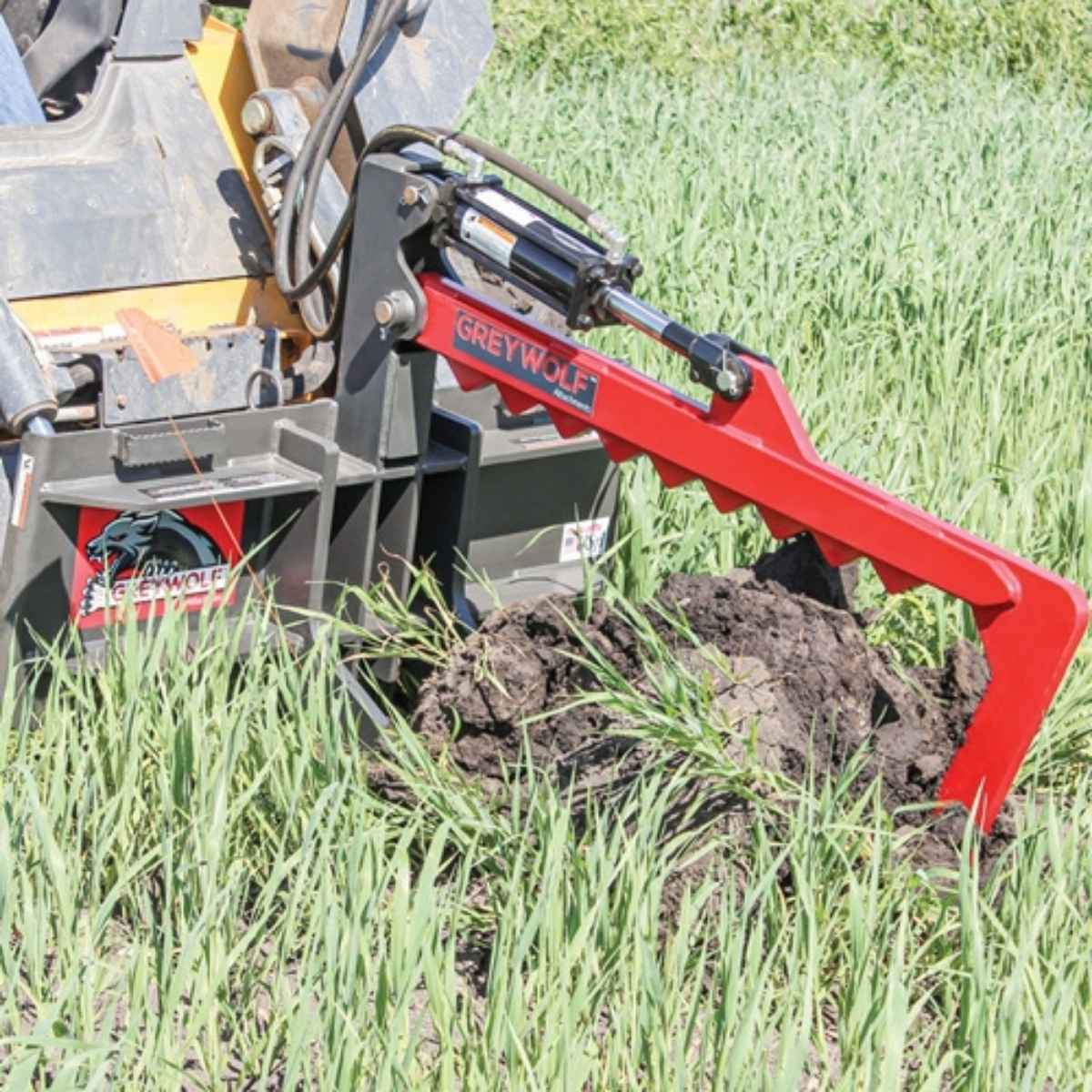 Red and gray Greywolf skid steer rock devil attachment labeled 'Greywolf' in a field