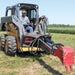 Person operating a skid steer loader with a red and grey greywolf backoe skid steer attachment in an open field.