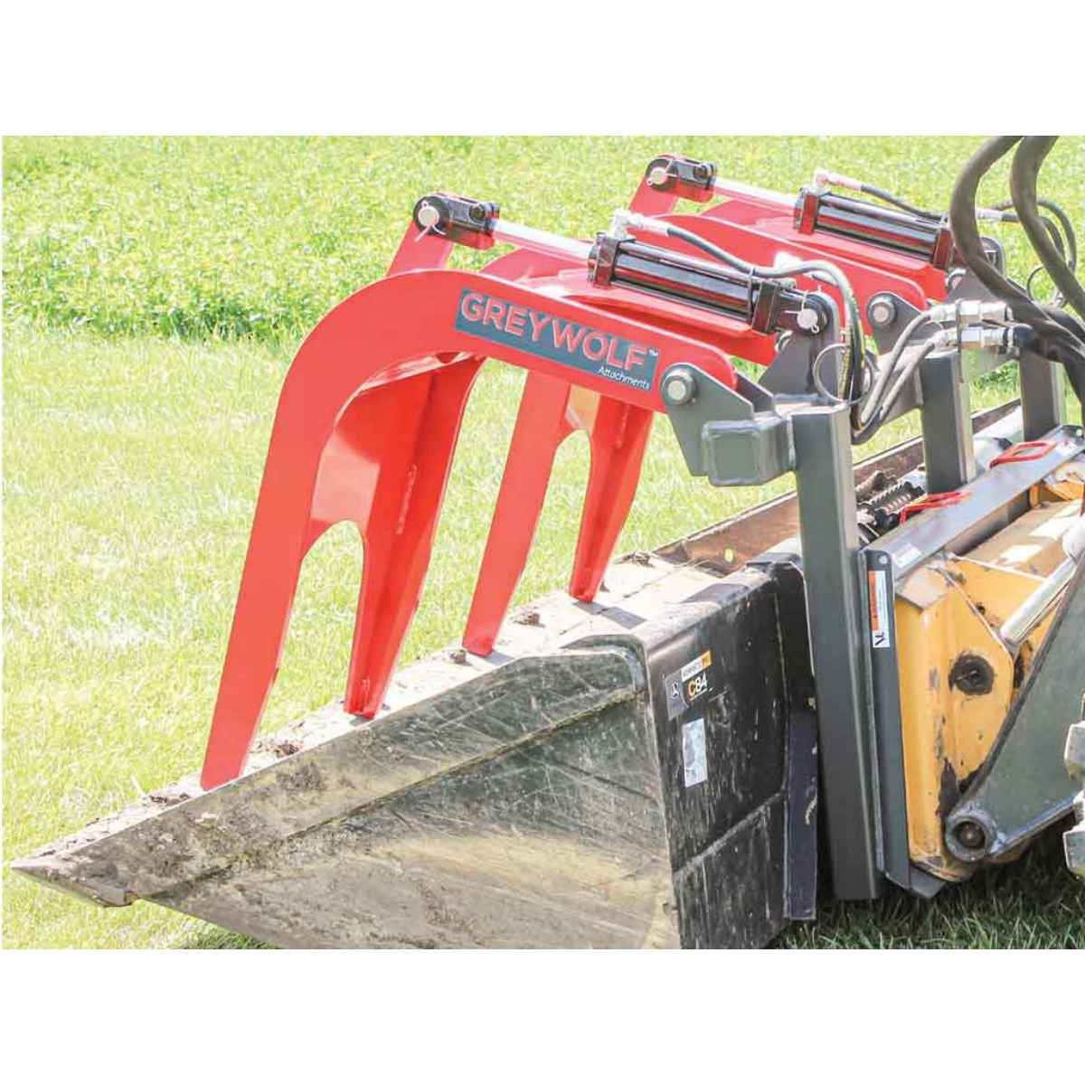 Red Greywolf quick attach grapple skid steer attachment on a green grass background