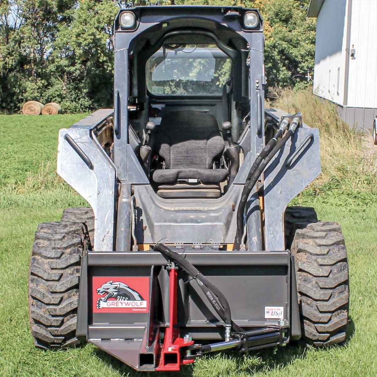 Skid steer loader with Greywolf skid steer tree puller attachment on a grassy field