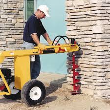 Person using a GroundHog HD99 one-man towable earth drill on The ground n front of a stone wall