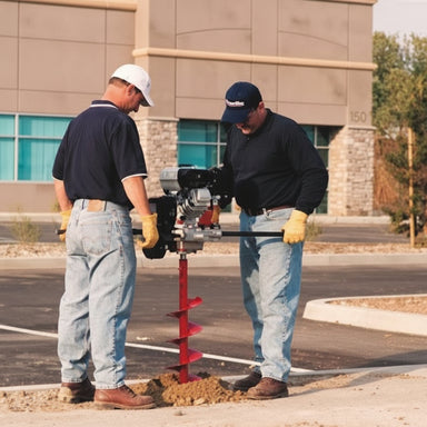 Two workers using a Ground Hog C-17-5 Earth Drill on a street.