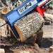 a blue iron and oak 24 ton skid steer mount log splitter holding a log with logs in the background