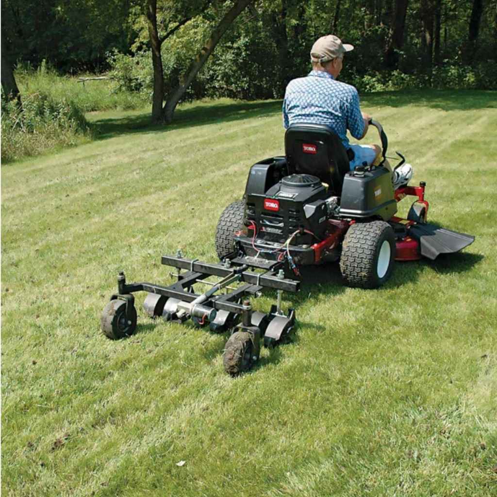 Man operating a riding lawn mower with a jrco 38 in tow behind hooker aerator on a grassy area.