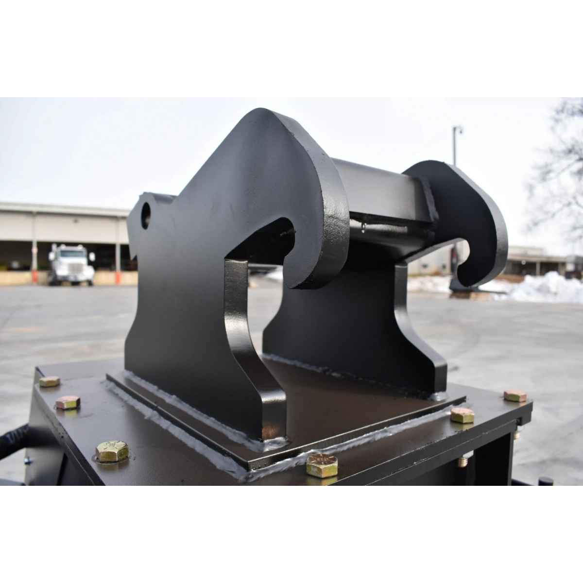 A heavy-duty black steel hydraulic clamp or loader hook attachment mounted on loflin fabrication mini excavator brush cutter, photographed outdoors in a paved industrial yard.