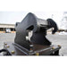 A heavy-duty black steel hydraulic clamp or loader hook attachment mounted on loflin fabrication mini excavator brush cutter, photographed outdoors in a paved industrial yard.
