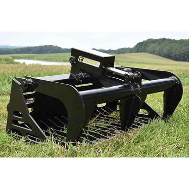 Black Loflin Mini Skid Steer Rock Grapple on a grassy field with trees and water in the background
