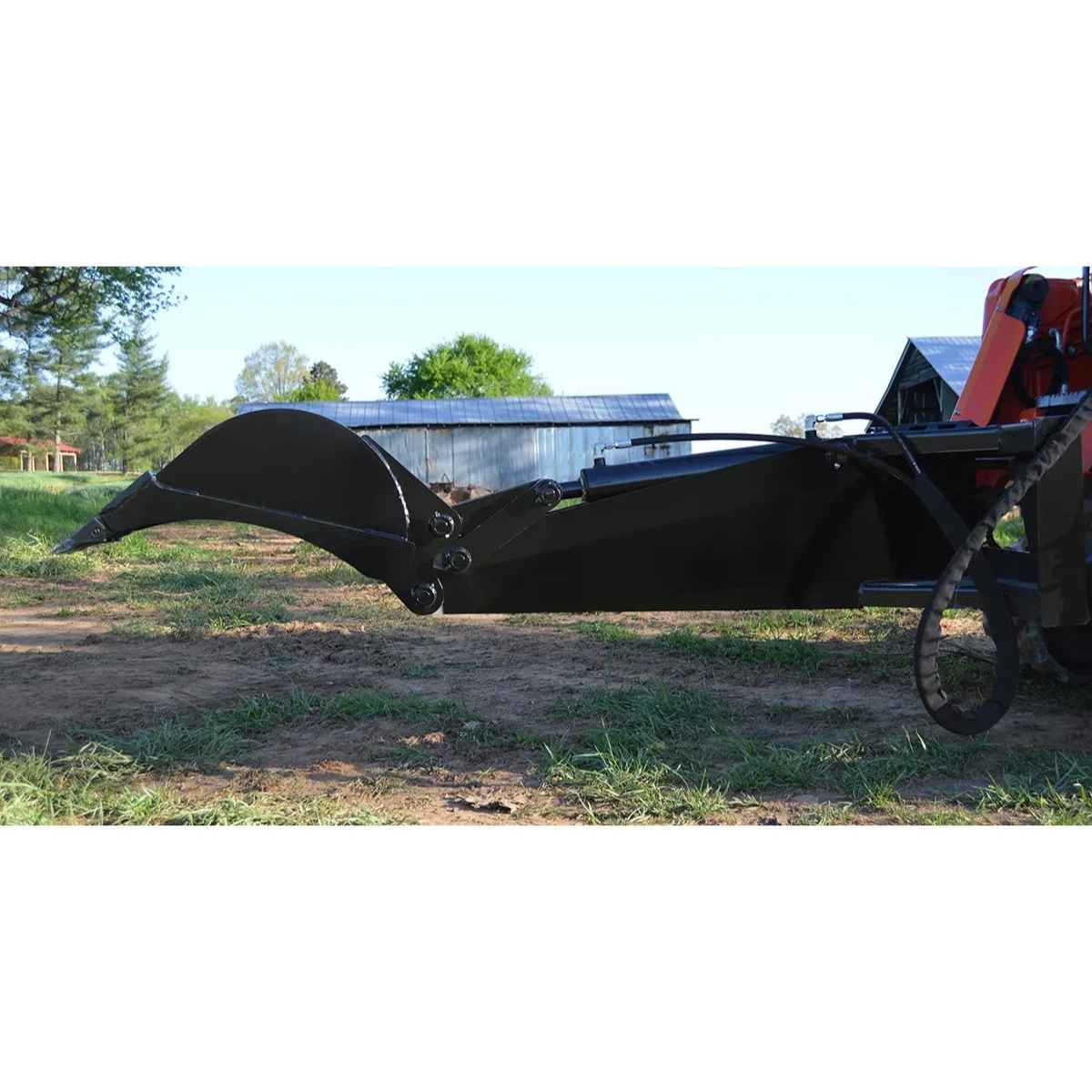 Large black Loflin Fabrication Backhoe attached to a vehicle in an outdoor setting with trees and a building in the background.