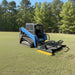 Red skid steer with a loflin fabrication severe duty brush cutter on a grassy field with trees in the background