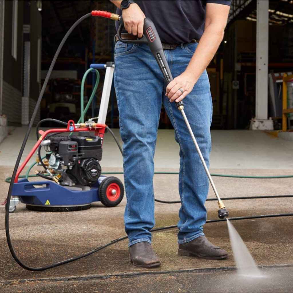 person using a blue and red makinex dual pressure cleaner on dirty concrete in a factory setting during the daytime outside.