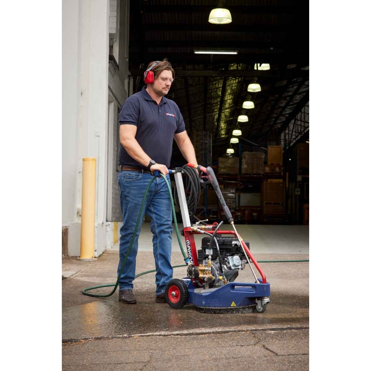 Man operating a Makinex 2200 PSi Dual pressure cleaner in a factory setting on an asphalt floor.