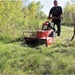 Man operating a red maxim brush cutter 26-in in a grassy outdoor area with trees in the background