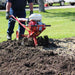 Person using a Maxim 26 inch tiller on a garden bed with grass in the background