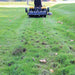 Black Maxim 36 inch lawn aerator tow behind attached to a yellow lawn mower on a grassy area
