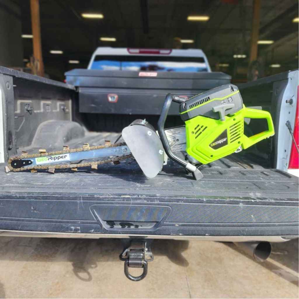 A green and black georipper trencher in the bed of a truck.
