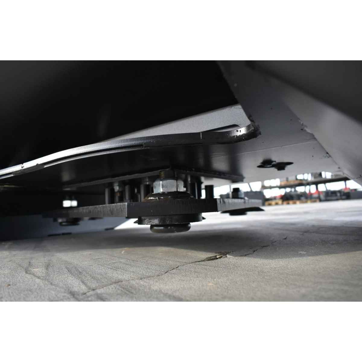 Close-up low-angle view of an undercarriage component of a loflin mini excavator brushcutter resting on a concrete floor in an industrial setting.