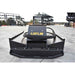 A black mini excavator brush cutter attachment by loflin fabrication, photographed from a front-facing perspective on an outdoor concrete yard with construction equipment in the background.