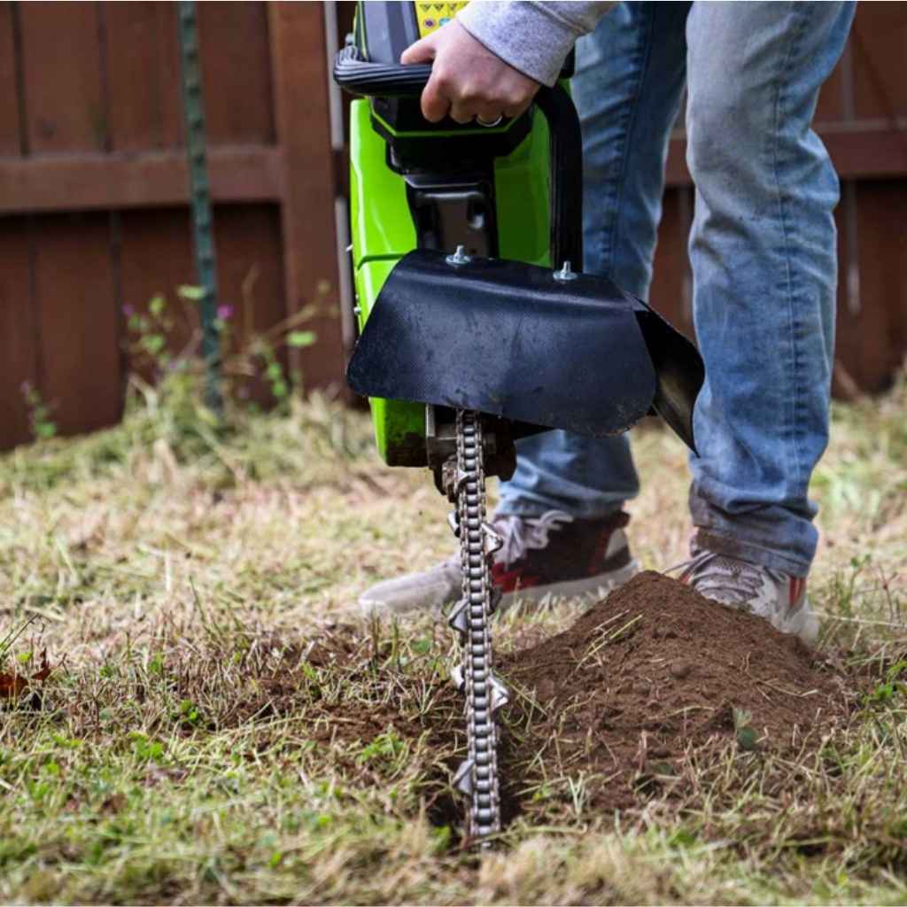 Person operating a mini trencher georipper for sale in a gassy backyard with a wooden fence in the background during the daytime