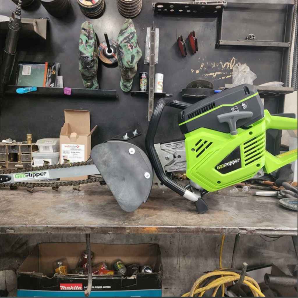 A Green and black georipper trencher for sale on a tool bench with grinder discs hanging on the wall in the background as well as various other tools.