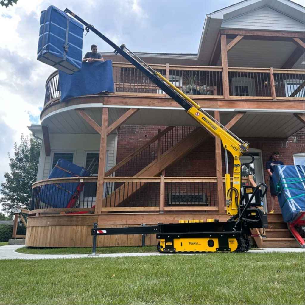 Yellow movex tt 270 stair climber lifting a large blue object on a grassy area in front of a house.