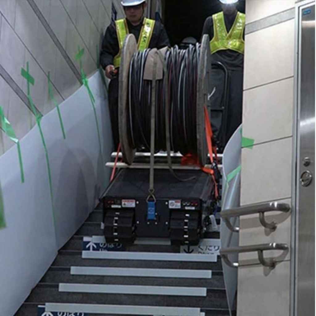 Person moving a cable reel with a movex tt 66 carrier on stairs, wearing safety gear.