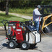 Red and black northstar 3500 psi hot water pressure washer 3.5 GPM on a driveway with a person using it in the background.