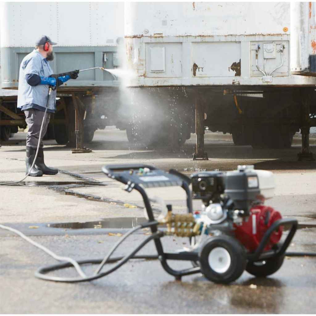 Person using a northstar 4200 psi 3.5  gpm pressure washer on a trailer with a power washer machine in the foreground.