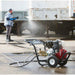 Person using a northstar 4200 psi 3.5  gpm pressure washer on a trailer with a power washer machine in the foreground.