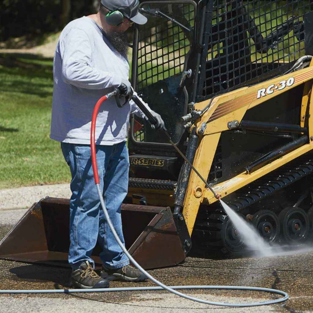 Person using a Northstar 3500 psi hot water pressure washer on a piece of construction equipment.