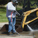 Person using a Northstar 3500 psi hot water pressure washer on a piece of construction equipment.