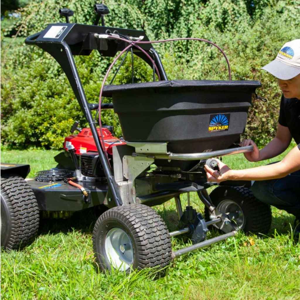 Person using a spyker ride on spreader attached to a lawn mower in a grassy area