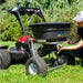 Person using a spyker ride on spreader attached to a lawn mower in a grassy area