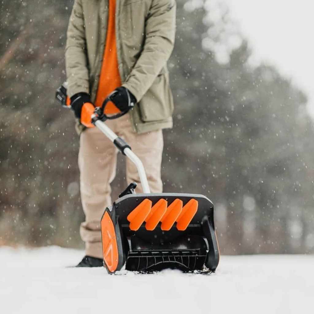 Person using an orange and black superhandy snow thrower pro in a snowy outdoor setting