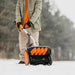 Person using an orange and black superhandy snow thrower pro in a snowy outdoor setting